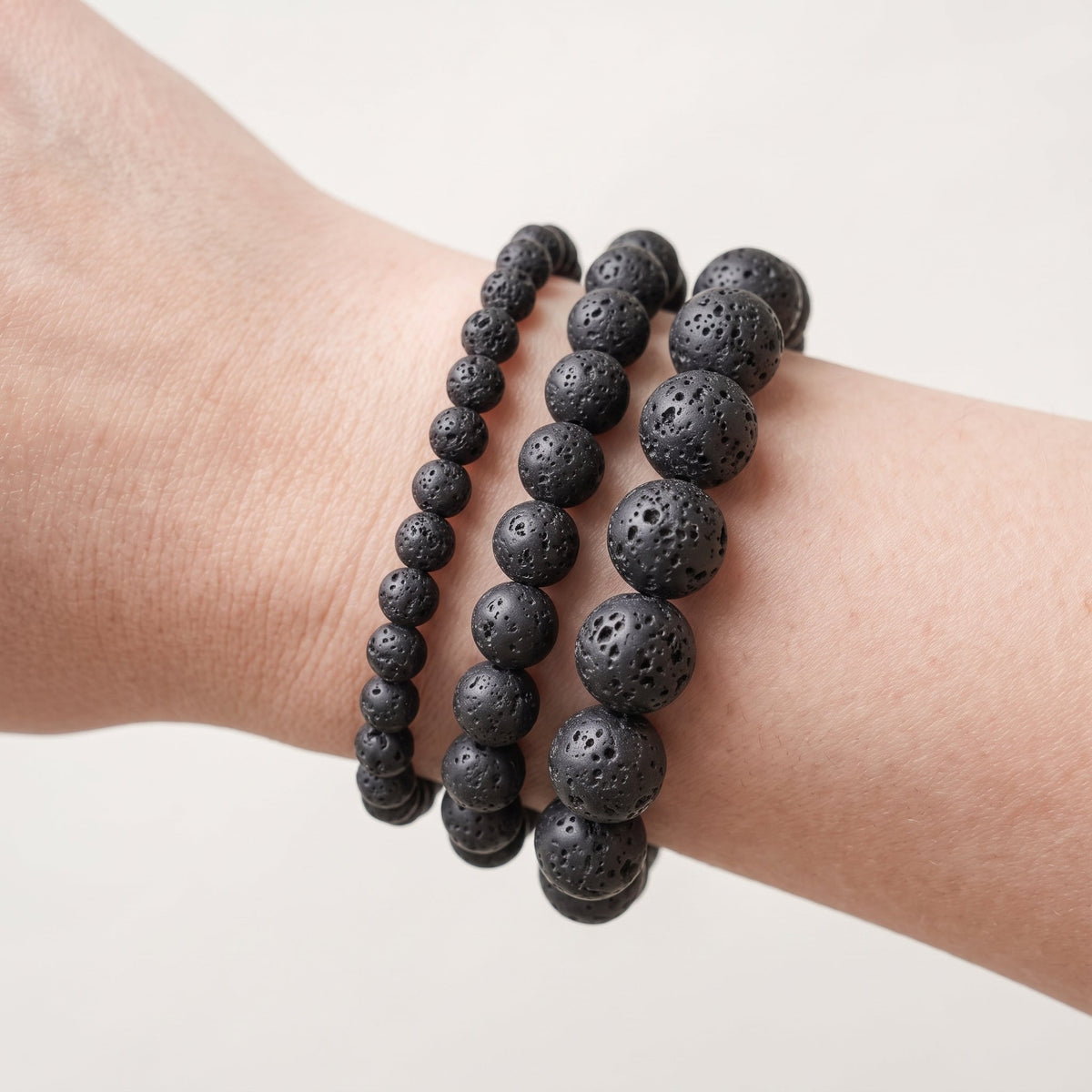 Trois bracelets en pierre de lave de diamètres différents, portés ensemble au poignet - visuel provisoire