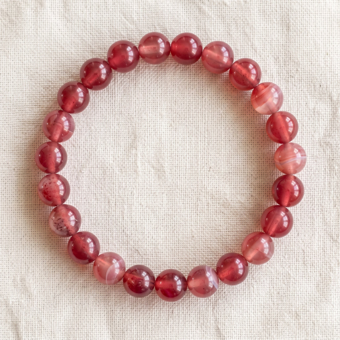 Bracelet en agate cerise : perles rondes de pierre naturelle de 8 mm sur elastique, sans interperle (variante temporaire), vu de dessus sur du lin ivoire - visuel provisoire
