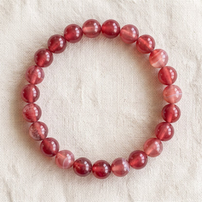 Bracelet en agate cerise : perles rondes de pierre naturelle de 8 mm sur elastique, sans interperle (variante temporaire), vu de dessus sur du lin ivoire - visuel provisoire