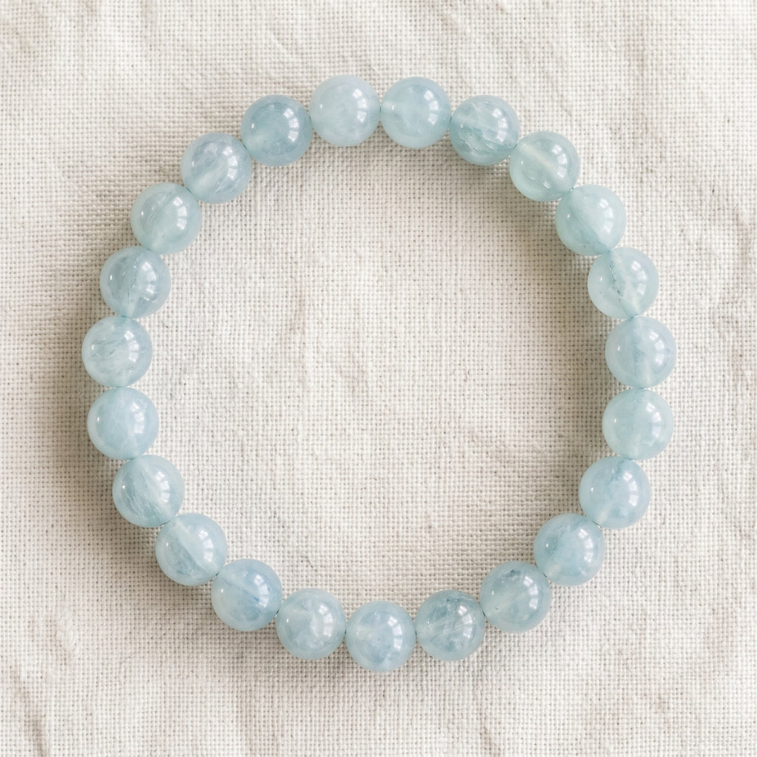 Bracelet en aigue marine : perles rondes de pierre naturelle de 8 mm sur elastique, sans interperle (variante temporaire), vu de dessus sur du lin ivoire - visuel provisoire