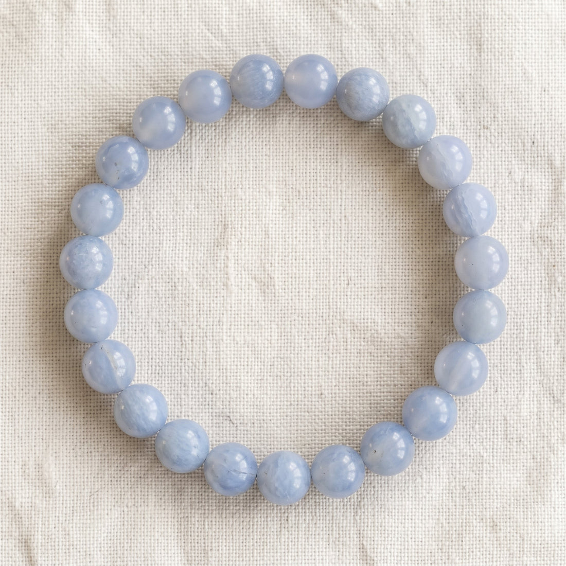 Bracelet en calcedoine bleue : perles rondes de pierre naturelle de 8 mm sur elastique, sans interperle (variante temporaire), vu de dessus sur du lin ivoire - visuel provisoire