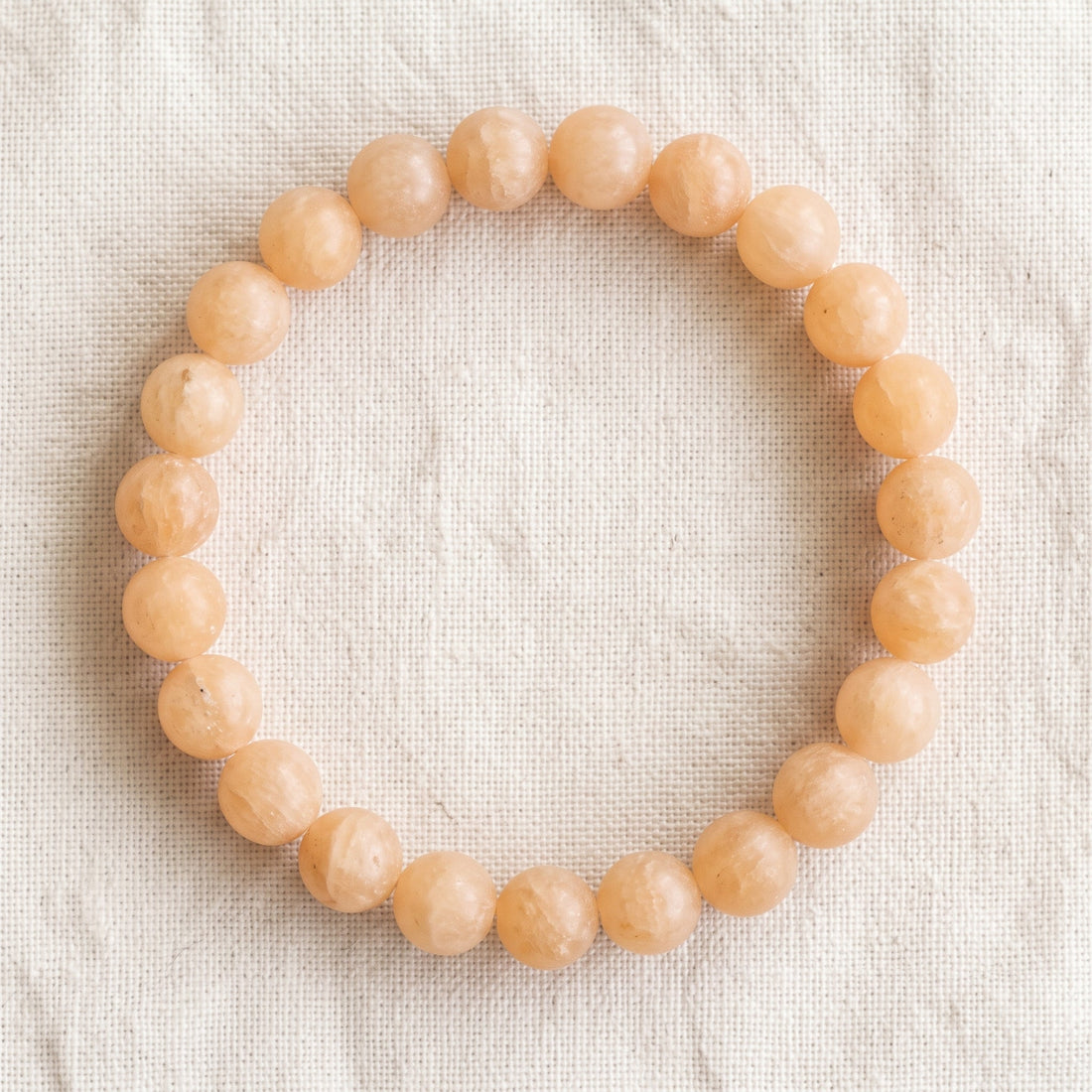 Bracelet en calcite orange : perles rondes de pierre naturelle de 8 mm sur elastique, sans interperle (variante temporaire), vu de dessus sur du lin ivoire - visuel provisoire