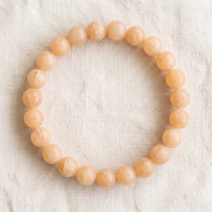Bracelet en calcite orange : perles rondes de pierre naturelle de 8 mm sur elastique, sans interperle (variante temporaire), vu de dessus sur du lin ivoire - visuel provisoire