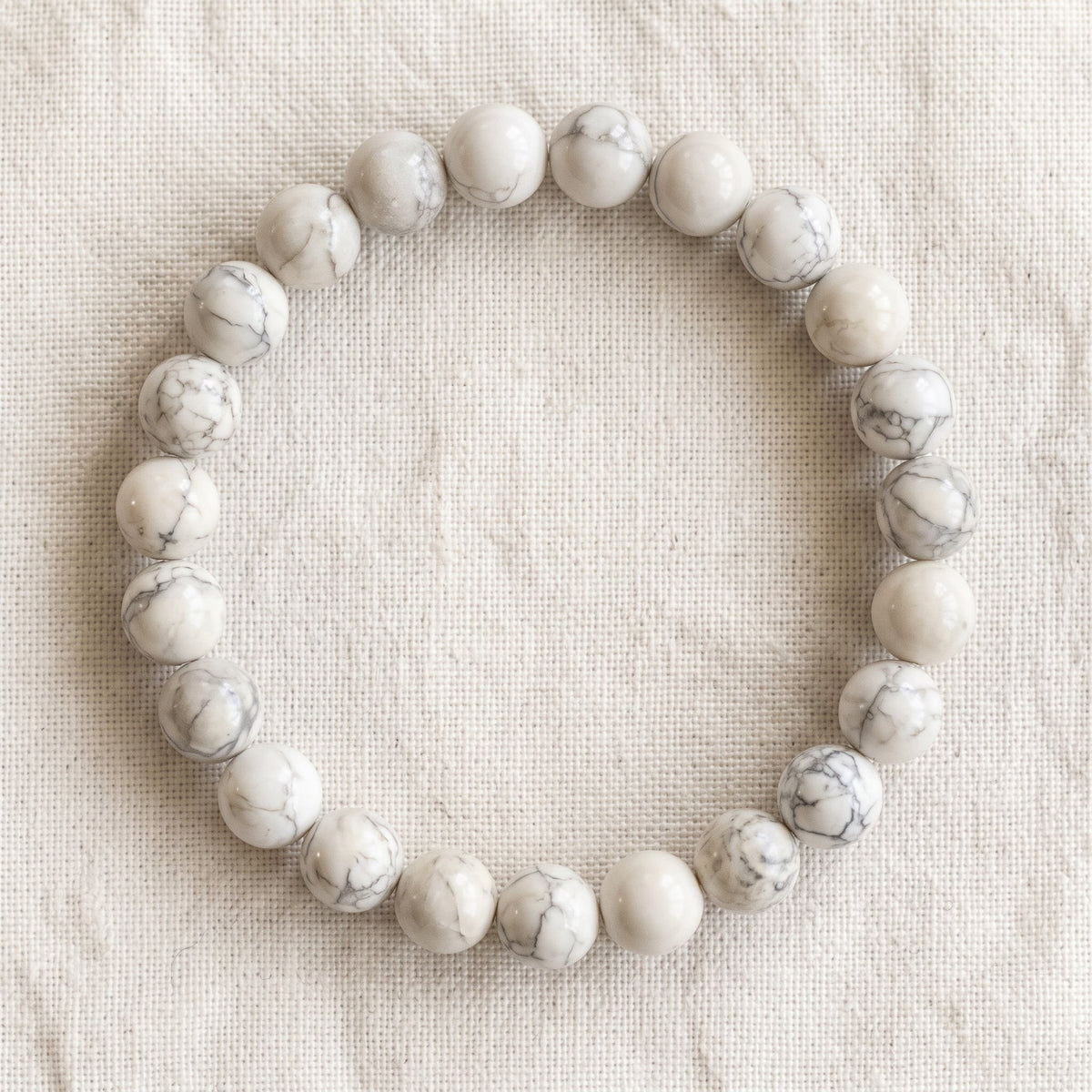 Bracelet en howlite : perles rondes de pierre naturelle de 8 mm sur elastique, sans interperle (variante temporaire), vu de dessus sur du lin ivoire - visuel provisoire