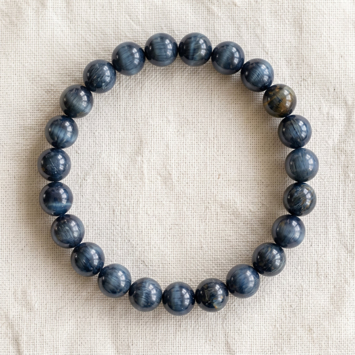 Bracelet en oeil de faucon : perles rondes de pierre naturelle de 8 mm sur elastique, sans interperle (variante temporaire), vu de dessus sur du lin ivoire - visuel provisoire