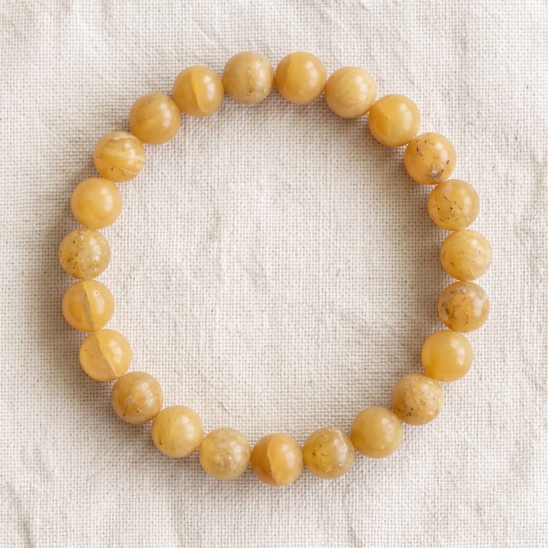 Bracelet en opale jaune : perles rondes de pierre naturelle de 8 mm sur elastique, sans interperle (variante temporaire), vu de dessus sur du lin ivoire - visuel provisoire