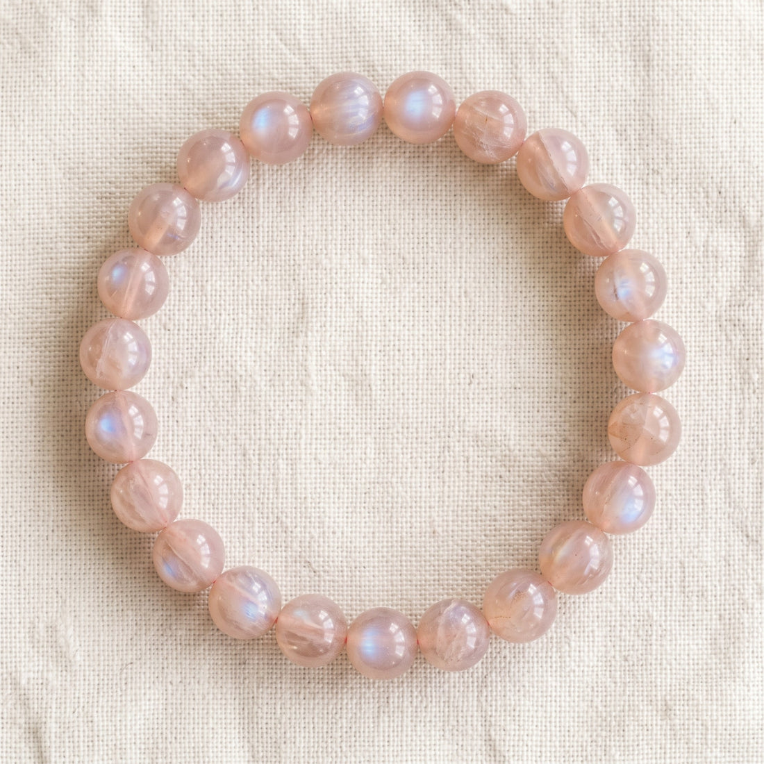 Bracelet en pierre de lune rose : perles rondes de pierre naturelle de 8 mm sur elastique, sans interperle (variante temporaire), vu de dessus sur du lin ivoire - visuel provisoire