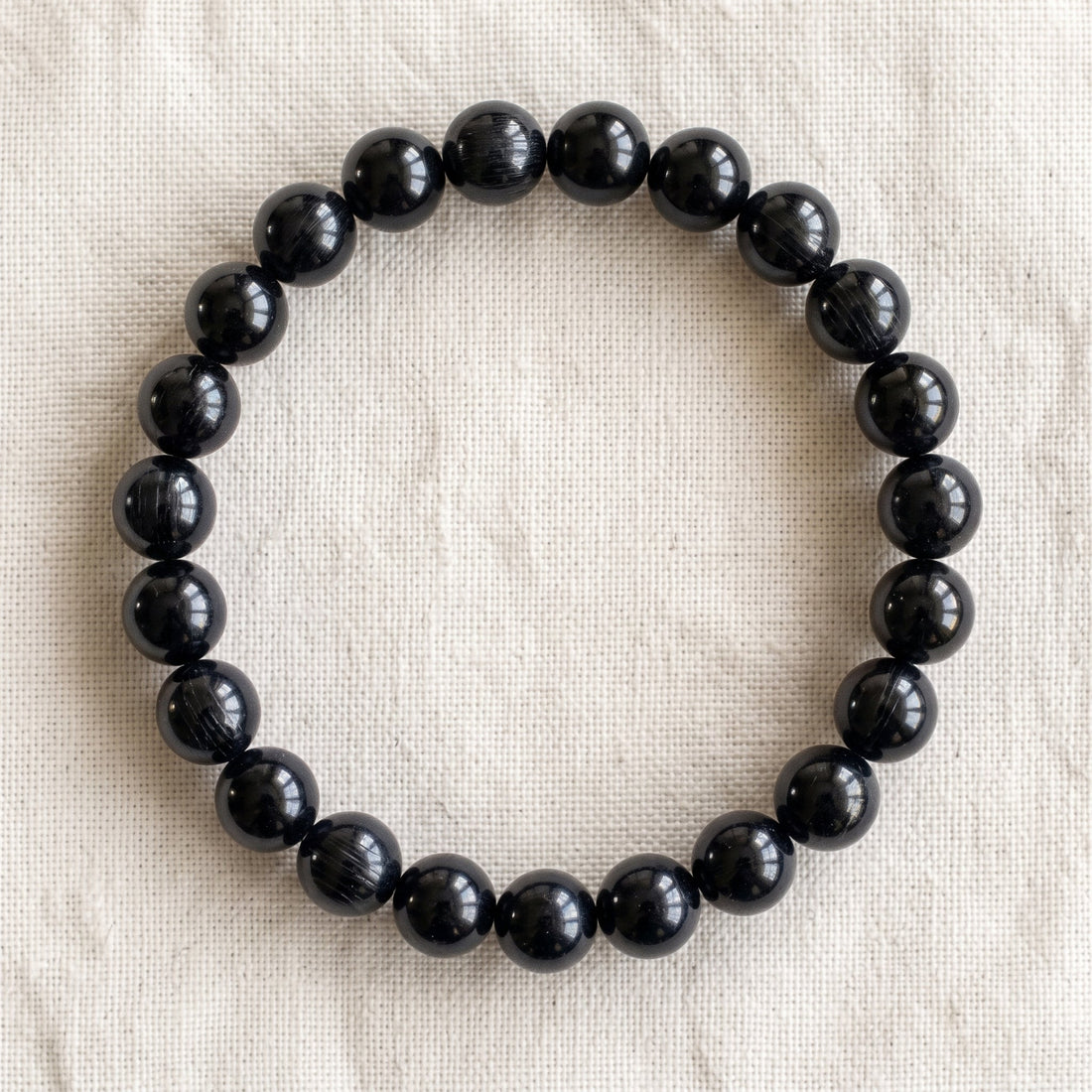 Bracelet en tourmaline noire : perles rondes de pierre naturelle de 8 mm sur elastique, sans interperle (variante temporaire), vu de dessus sur du lin ivoire - visuel provisoire