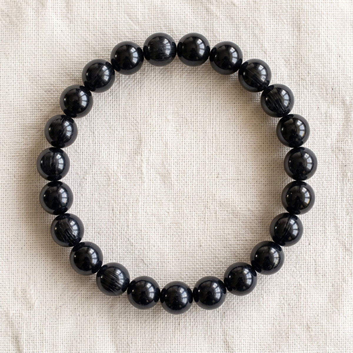Bracelet en tourmaline noire : perles rondes de pierre naturelle de 8 mm sur elastique, sans interperle (variante temporaire), vu de dessus sur du lin ivoire - visuel provisoire