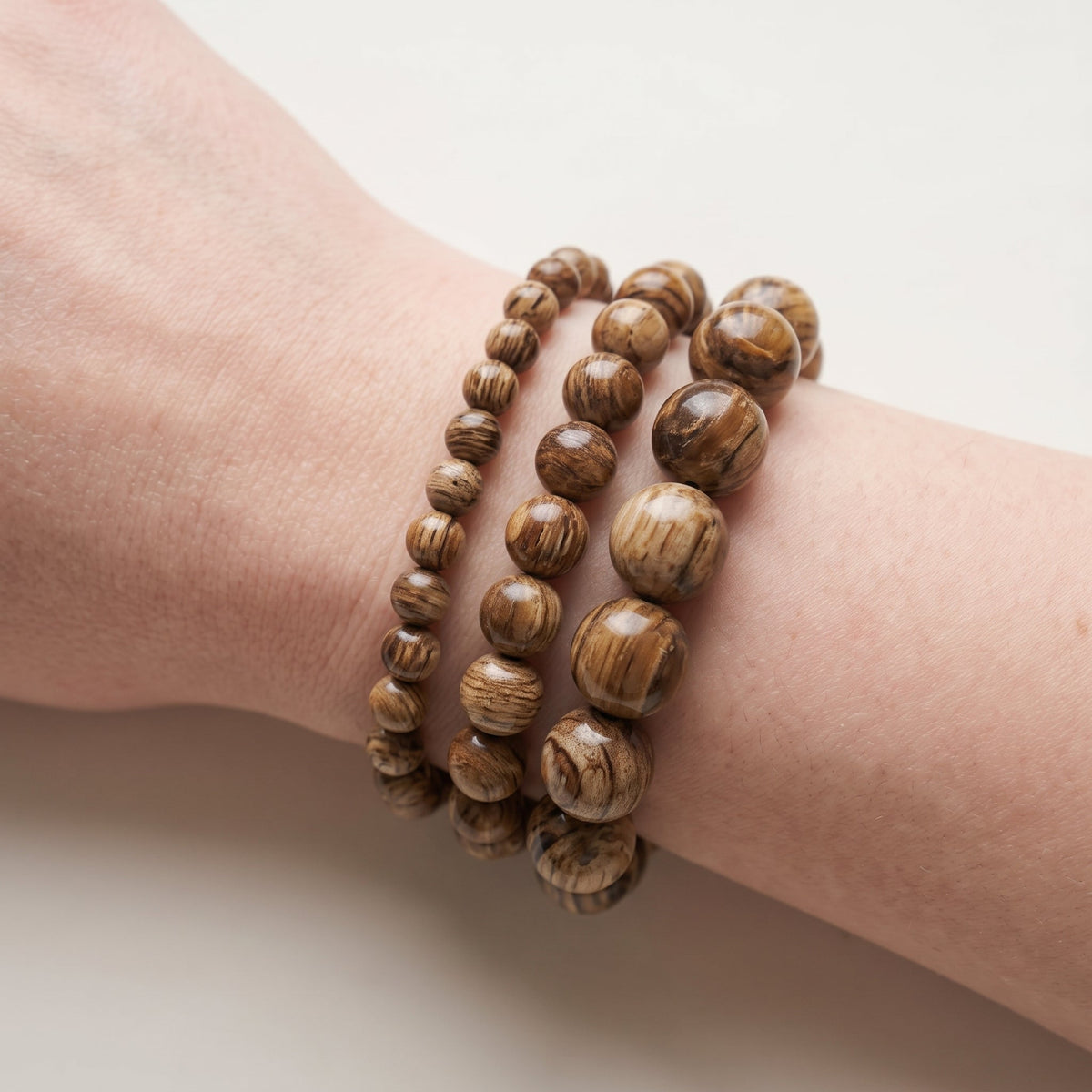 Trois bracelets en bois fossilisé de diamètres différents, portés ensemble au poignet - visuel provisoire