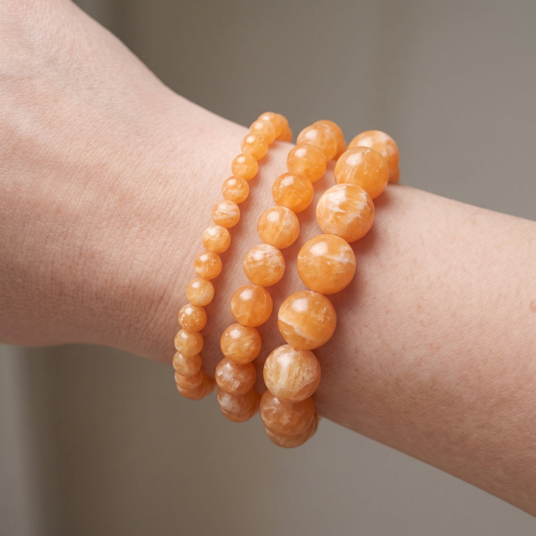 Trois bracelets en calcite orange de diamètres différents, portés ensemble au poignet - visuel provisoire