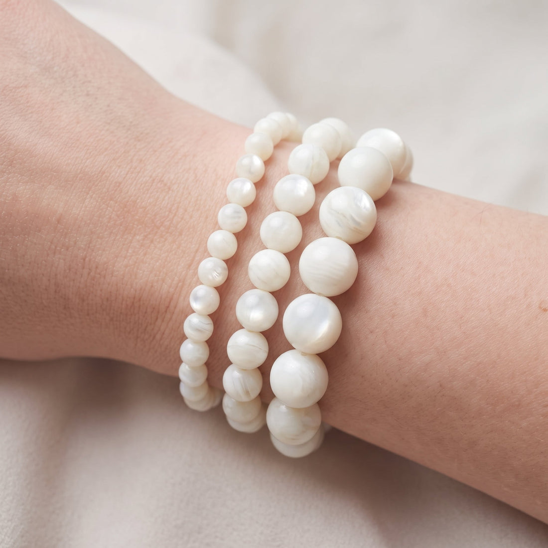 Trois bracelets en nacre blanche (perles boule) de diamètres différents, portés ensemble au poignet - visuel provisoire