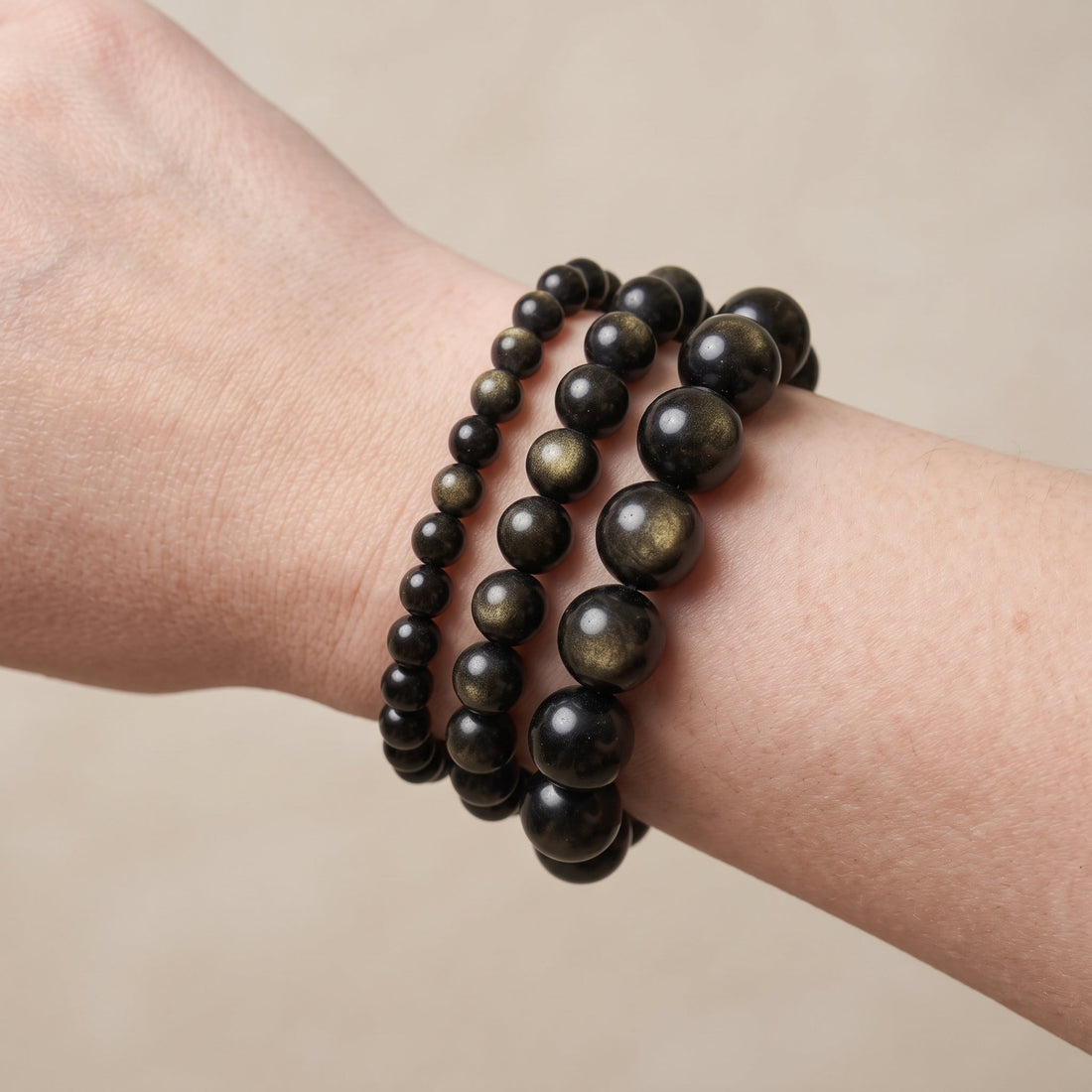 Trois bracelets en obsidienne dorée de diamètres différents, portés ensemble au poignet - visuel provisoire