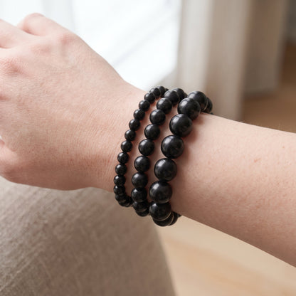 Trois bracelets en obsidienne noire de diamètres différents, portés ensemble au poignet - visuel provisoire