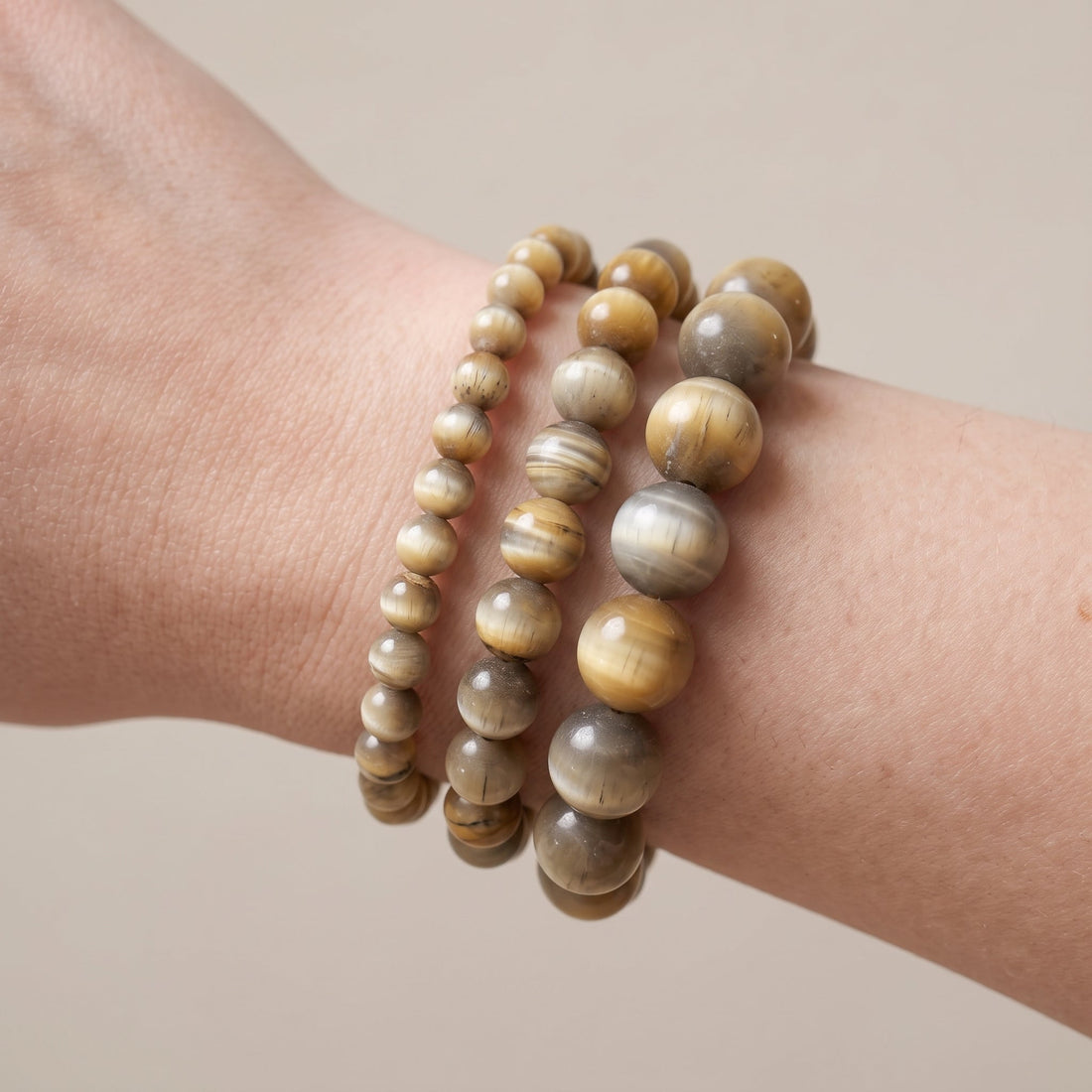 Trois bracelets en œil de tigre blanc de diamètres différents, portés ensemble au poignet - visuel provisoire