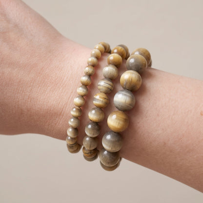 Trois bracelets en œil de tigre blanc de diamètres différents, portés ensemble au poignet - visuel provisoire
