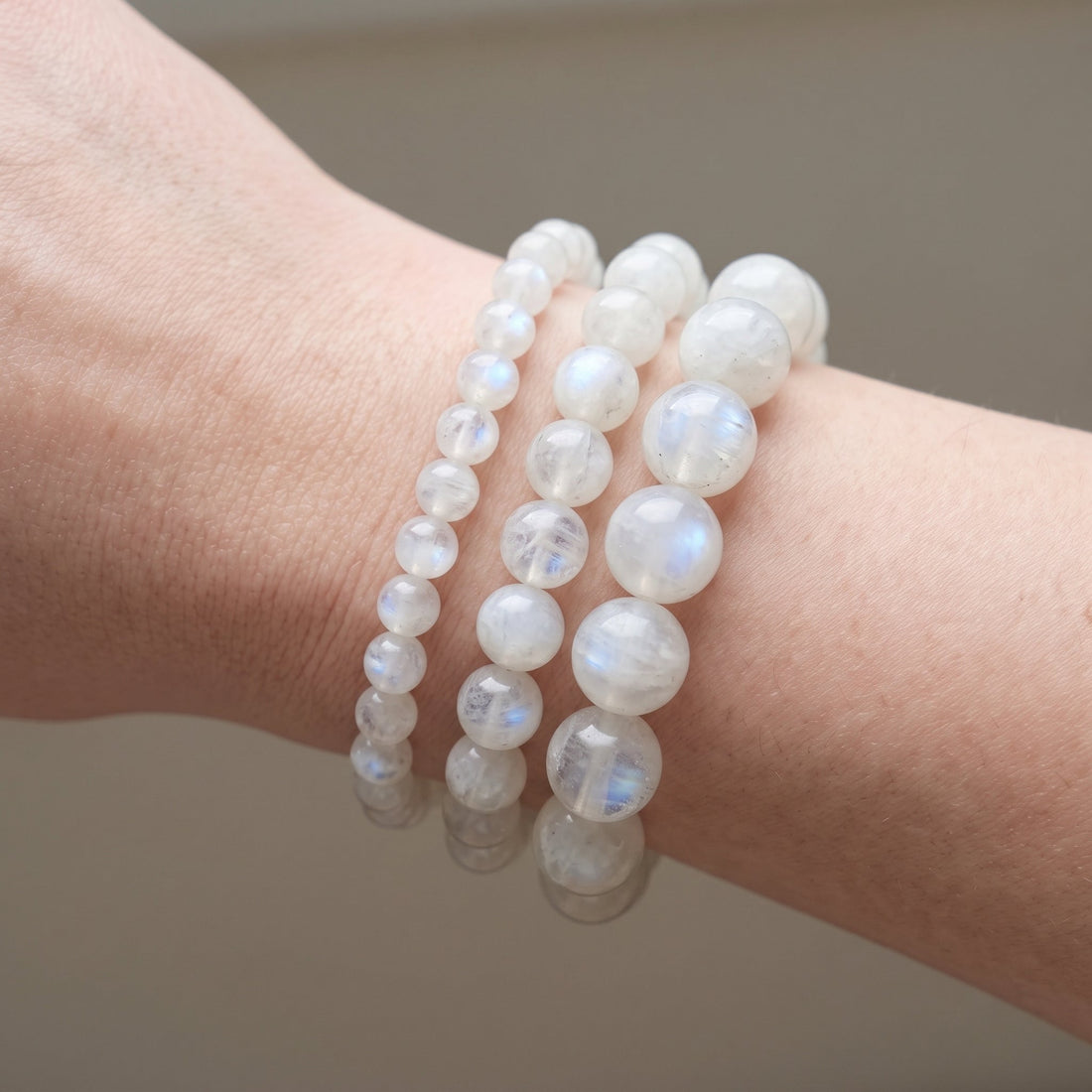 Trois bracelets en pierre de lune blanche de diamètres différents, portés ensemble au poignet - visuel provisoire