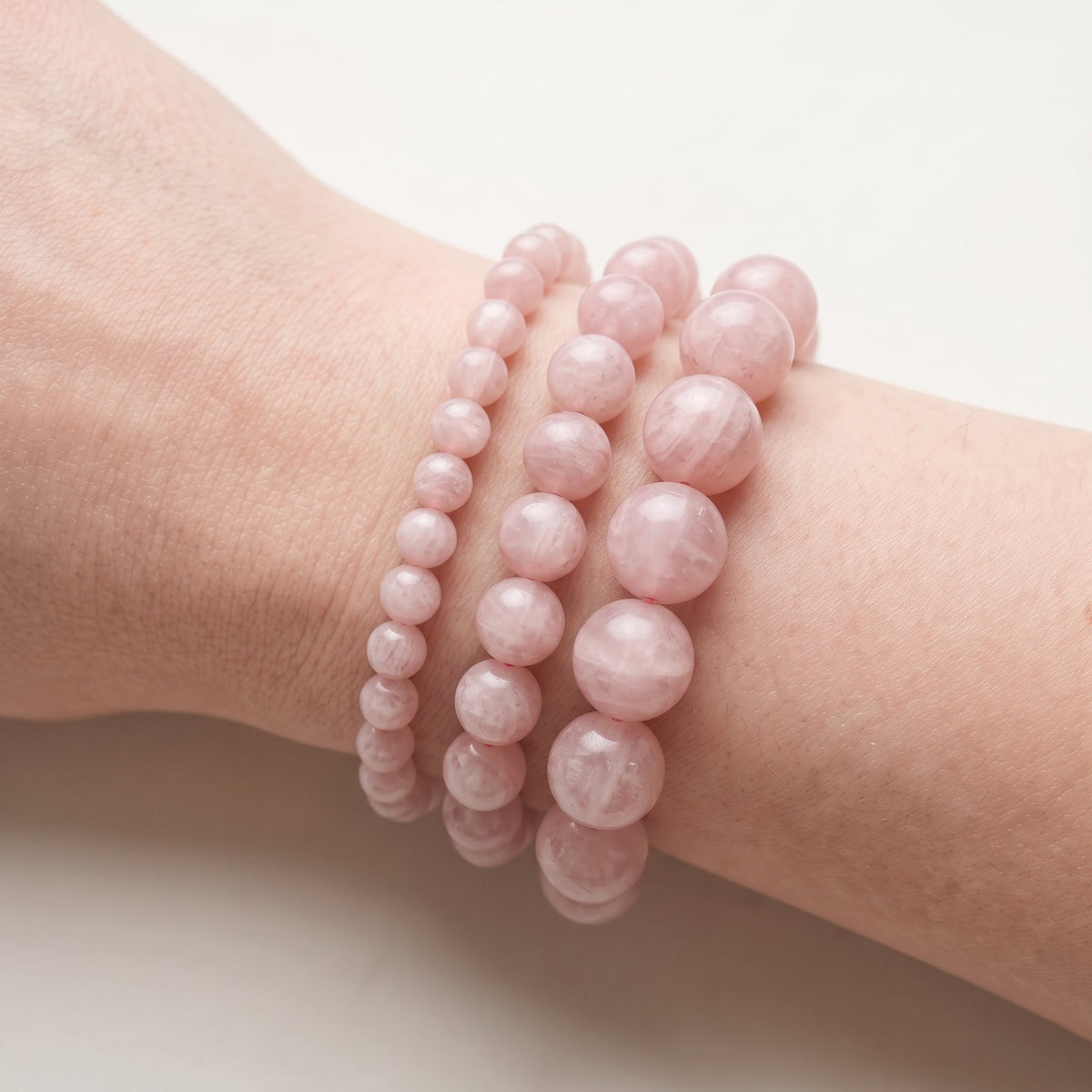 Trois bracelets en pierre de lune rose de diamètres différents, portés ensemble au poignet - visuel provisoire