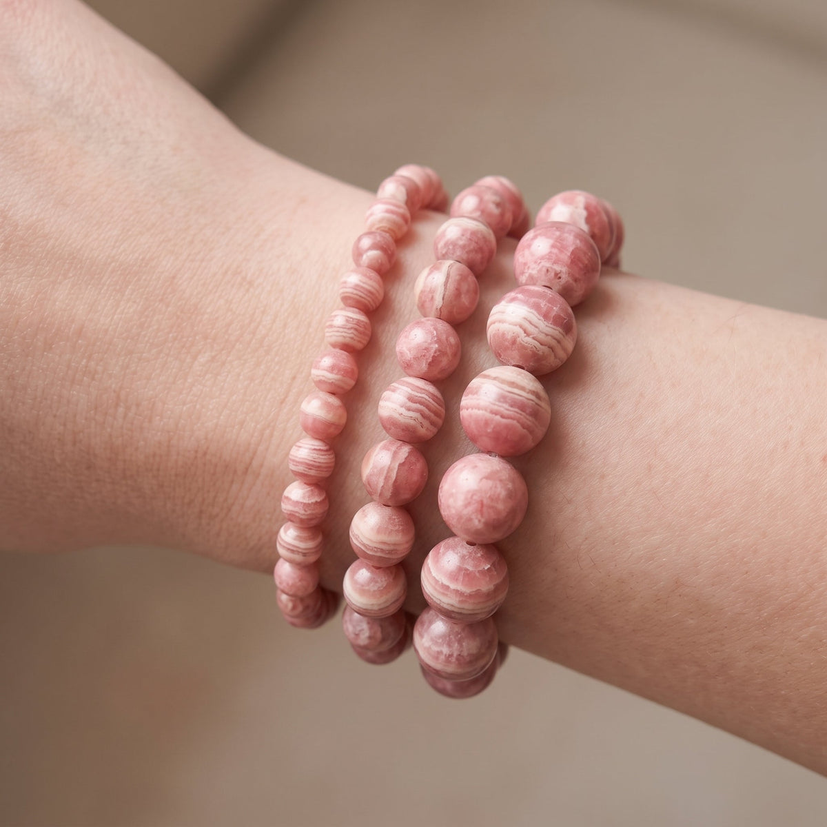 Trois bracelets en rhodochrosite de diamètres différents, portés ensemble au poignet - visuel provisoire