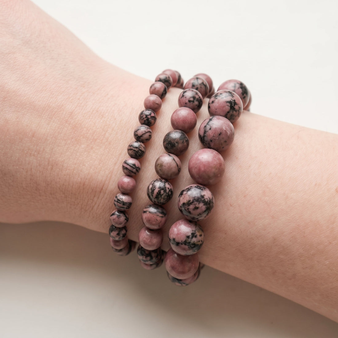 Trois bracelets en rhodonite de diamètres différents, portés ensemble au poignet - visuel provisoire
