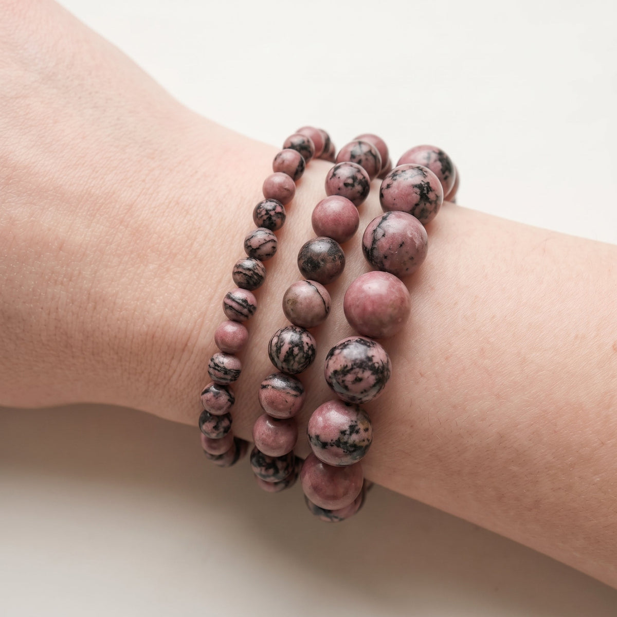 Trois bracelets en rhodonite de diamètres différents, portés ensemble au poignet - visuel provisoire