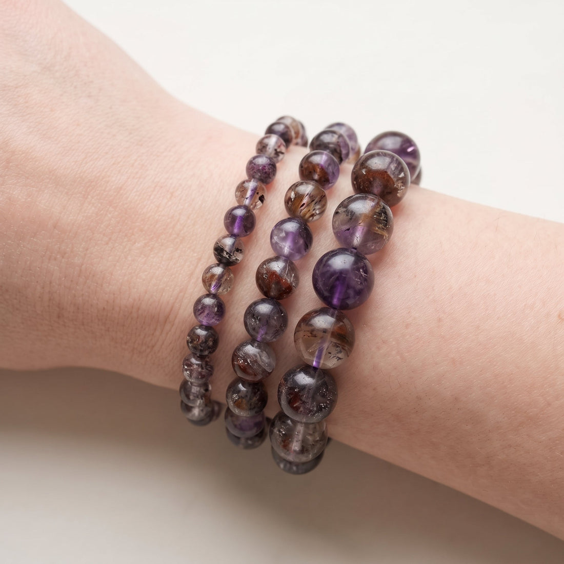 Trois bracelets en super seven de diamètres différents, portés ensemble au poignet - visuel provisoire