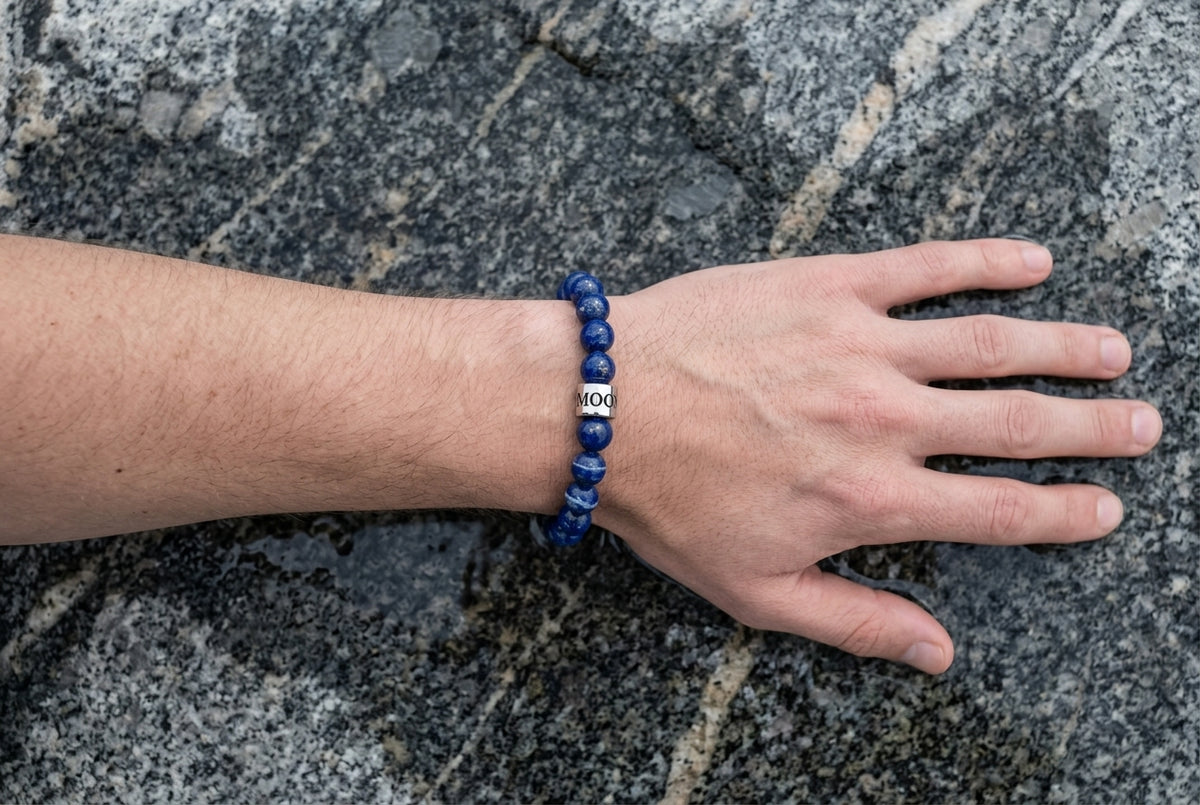 Main posee a plat sur une dalle de granit veinee de quartz, bracelet en perles de pierre naturelle bleue au poignet, vue de dessus — visuel provisoire