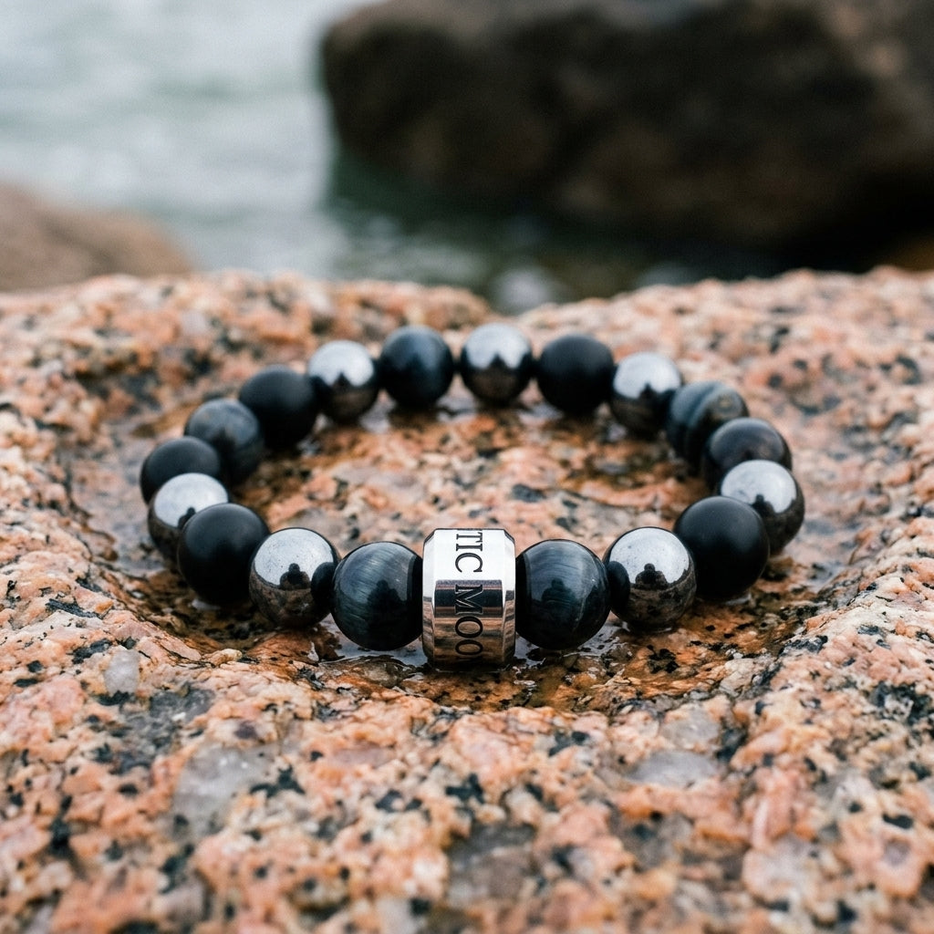 Bracelet Le Rempart en onyx, hematite et oeil de faucon, pose dans un creux de granit rose sur la cote bretonne - visuel provisoire