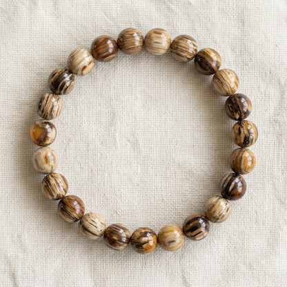 Bracelet en bois fossilisé : perles rondes de pierre naturelle de 8 mm sur elastique, sans interperle (variante temporaire), vu de dessus sur du lin ivoire - visuel provisoire