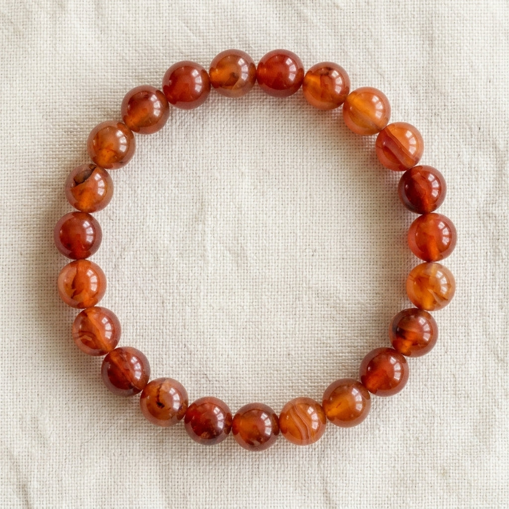 Bracelet en cornaline : perles rondes de pierre naturelle de 8 mm sur elastique, sans interperle (variante temporaire), vu de dessus sur du lin ivoire - visuel provisoire