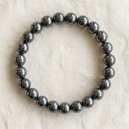 Bracelet en hematite : perles rondes de pierre naturelle de 8 mm sur elastique, sans interperle (variante temporaire), vu de dessus sur du lin ivoire - visuel provisoire