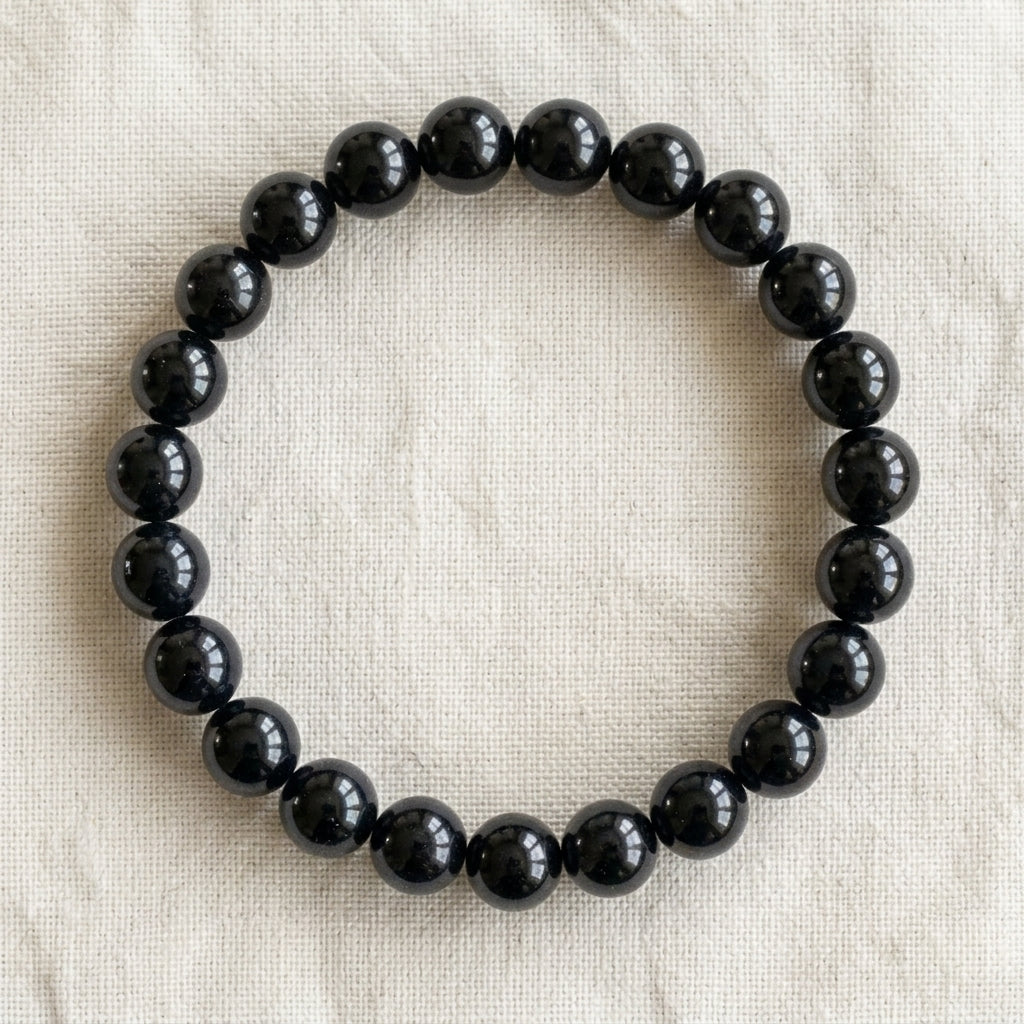 Bracelet en obsidienne noire : perles rondes de pierre naturelle de 8 mm sur elastique, sans interperle (variante temporaire), vu de dessus sur du lin ivoire - visuel provisoire
