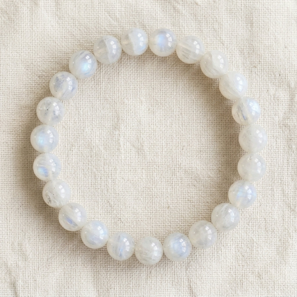 Bracelet en pierre de lune blanche : perles rondes de pierre naturelle de 8 mm sur elastique, sans interperle (variante temporaire), vu de dessus sur du lin ivoire - visuel provisoire