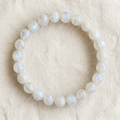 Bracelet en pierre de lune blanche : perles rondes de pierre naturelle de 8 mm sur elastique, sans interperle (variante temporaire), vu de dessus sur du lin ivoire - visuel provisoire