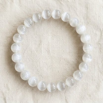Bracelet en sélénite : perles rondes de pierre naturelle de 8 mm sur elastique, sans interperle (variante temporaire), vu de dessus sur du lin ivoire - visuel provisoire