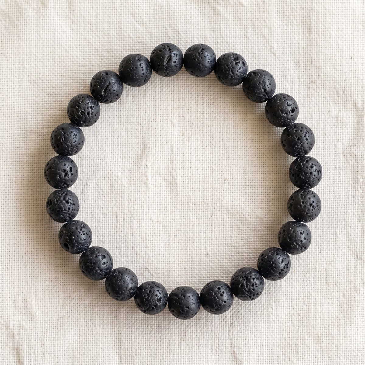 Bracelet en pierre de lave : perles rondes de pierre naturelle de 8 mm sur elastique, sans interperle (variante temporaire), vu de dessus sur du lin ivoire - visuel provisoire