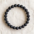 Bracelet en pierre de lave : perles rondes de pierre naturelle de 8 mm sur elastique, sans interperle (variante temporaire), vu de dessus sur du lin ivoire - visuel provisoire